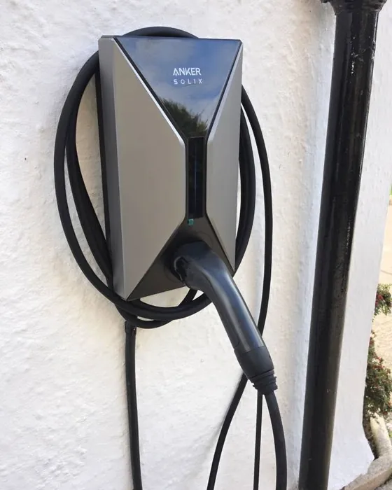 Anker Solix V1 tethered EV charger with its cable coiled on a white rendered wall beside a black downpipe, in the Wirral